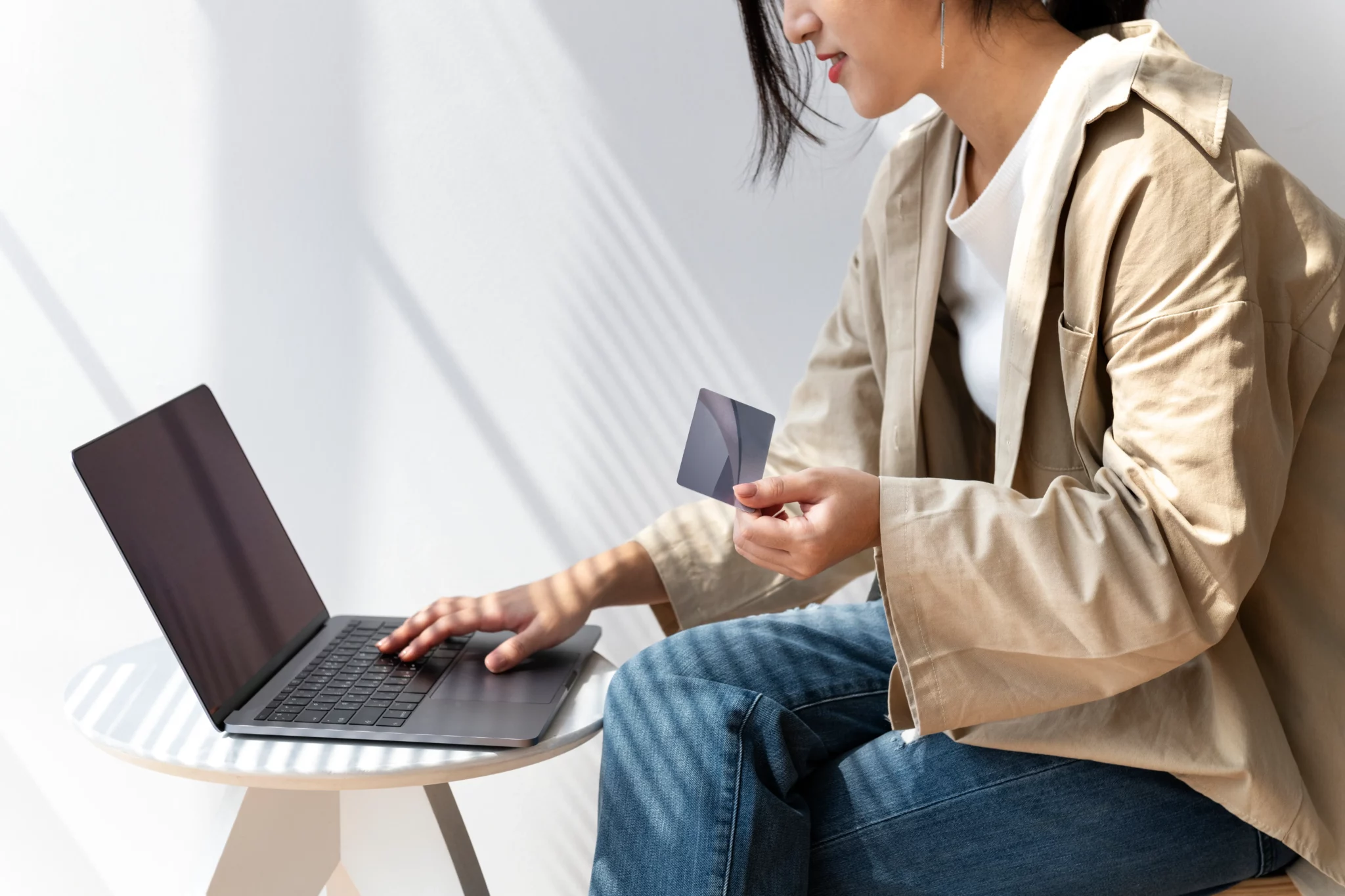 Seorang wanita memegang kartu kredit sambil bermain laptop
